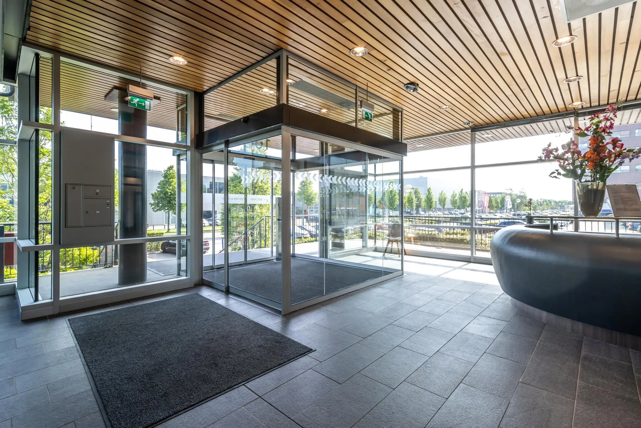 Ingang van een modern kantoorgebouw met glazen draaideur en receptiebalie aan de Rijnzathe.