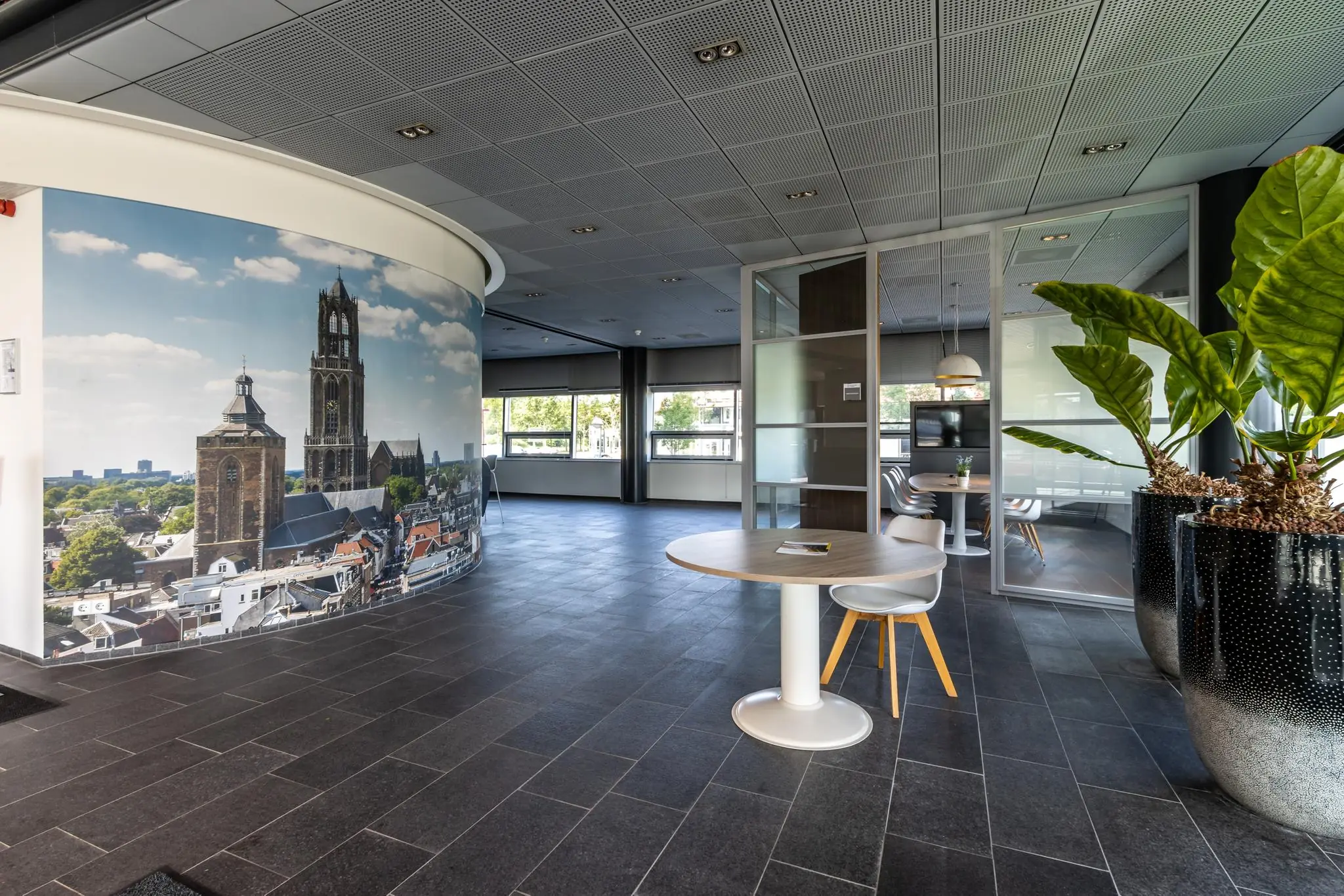 Moderne kantoorlobby met wanddecoratie van de Domtoren in Utrecht, zitgedeelte en grote planten in sierpotten.