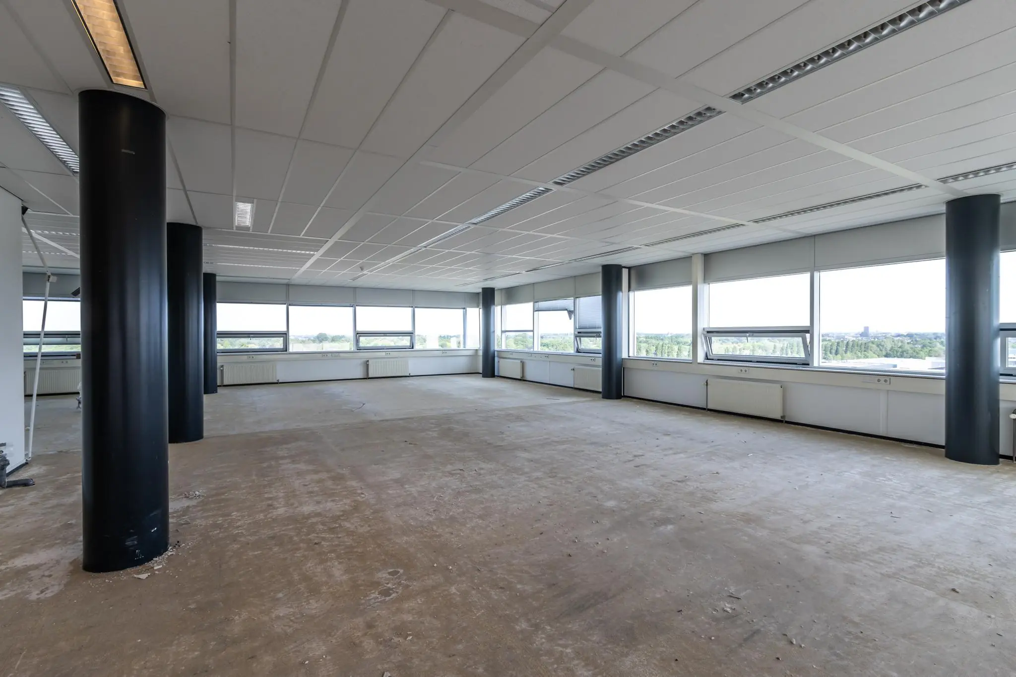 Leeg kantoorpand aan de Rijnzathe met grote ramen en uitzicht op groen landschap.