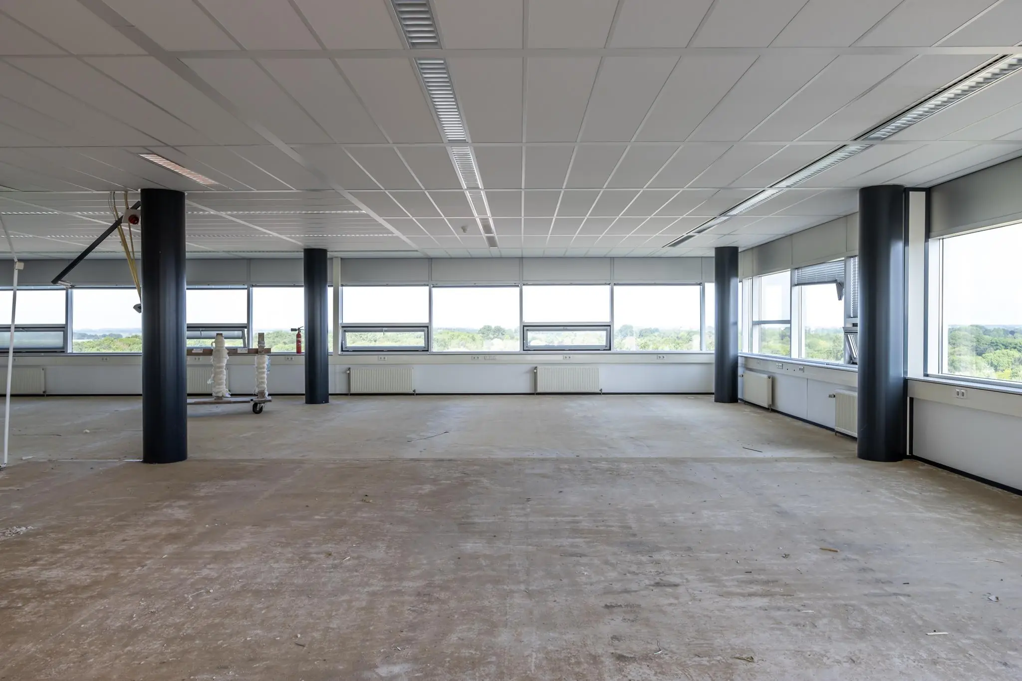 Leeg en ongebruikt kantoorruimte in gebouw Rijnzathe met grote ramen en uitzicht op groen.