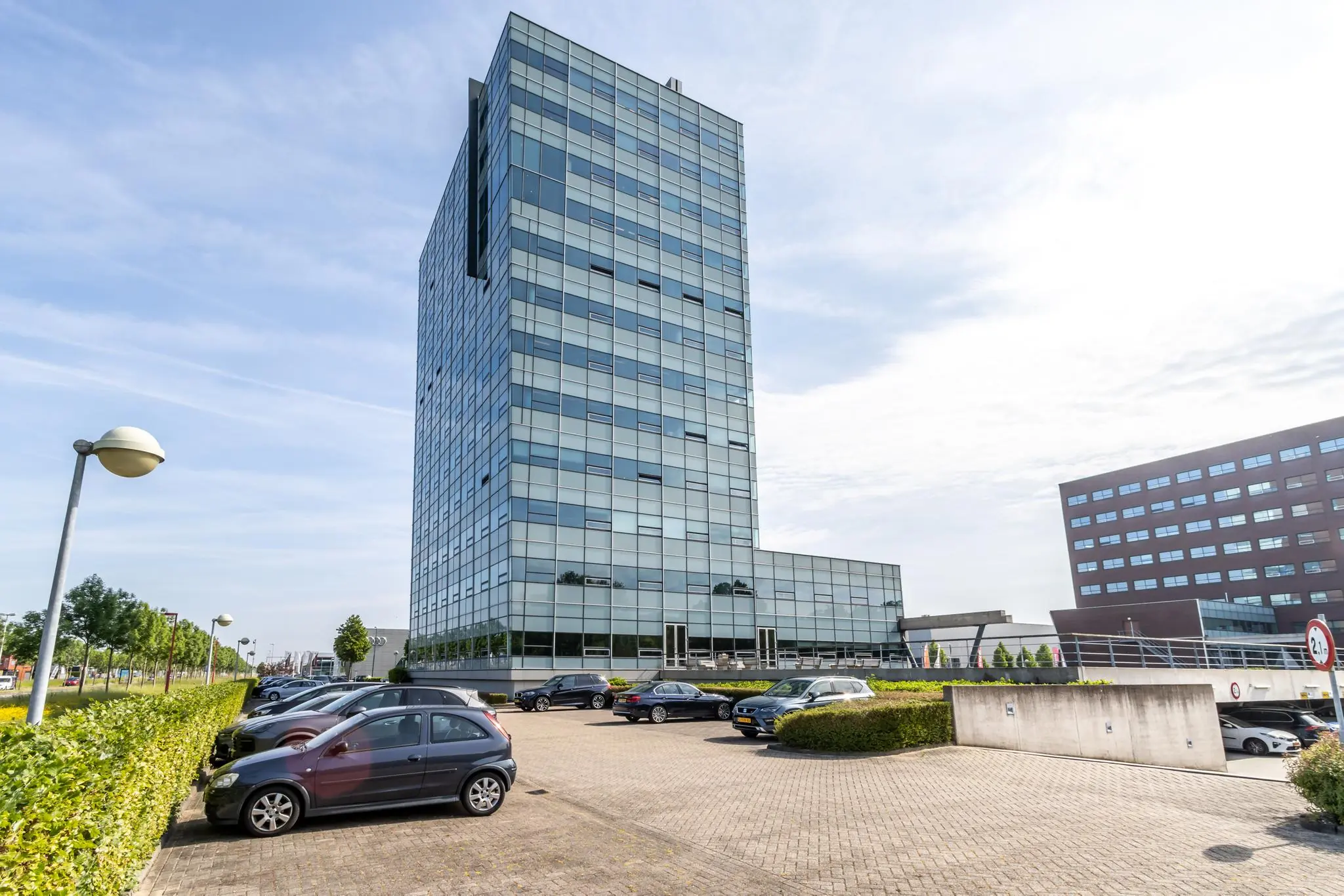 Modern kantoorgebouw aan de Rijnzathe met omliggend parkeerterrein op een zonnige dag.
