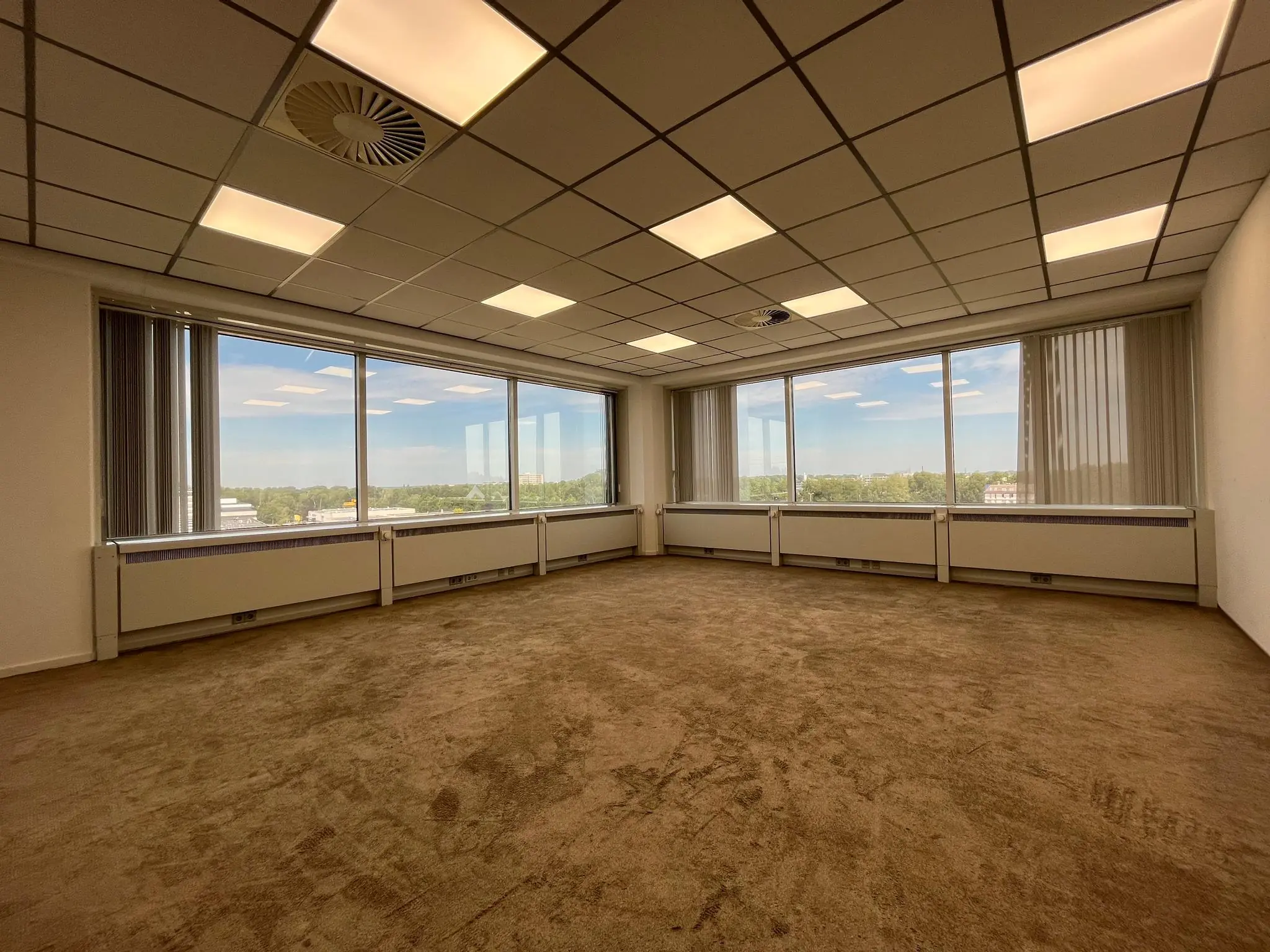 Leeg kantoor met tapijtvloer en grote ramen aan de Savannahweg met uitzicht op een groen landschap.