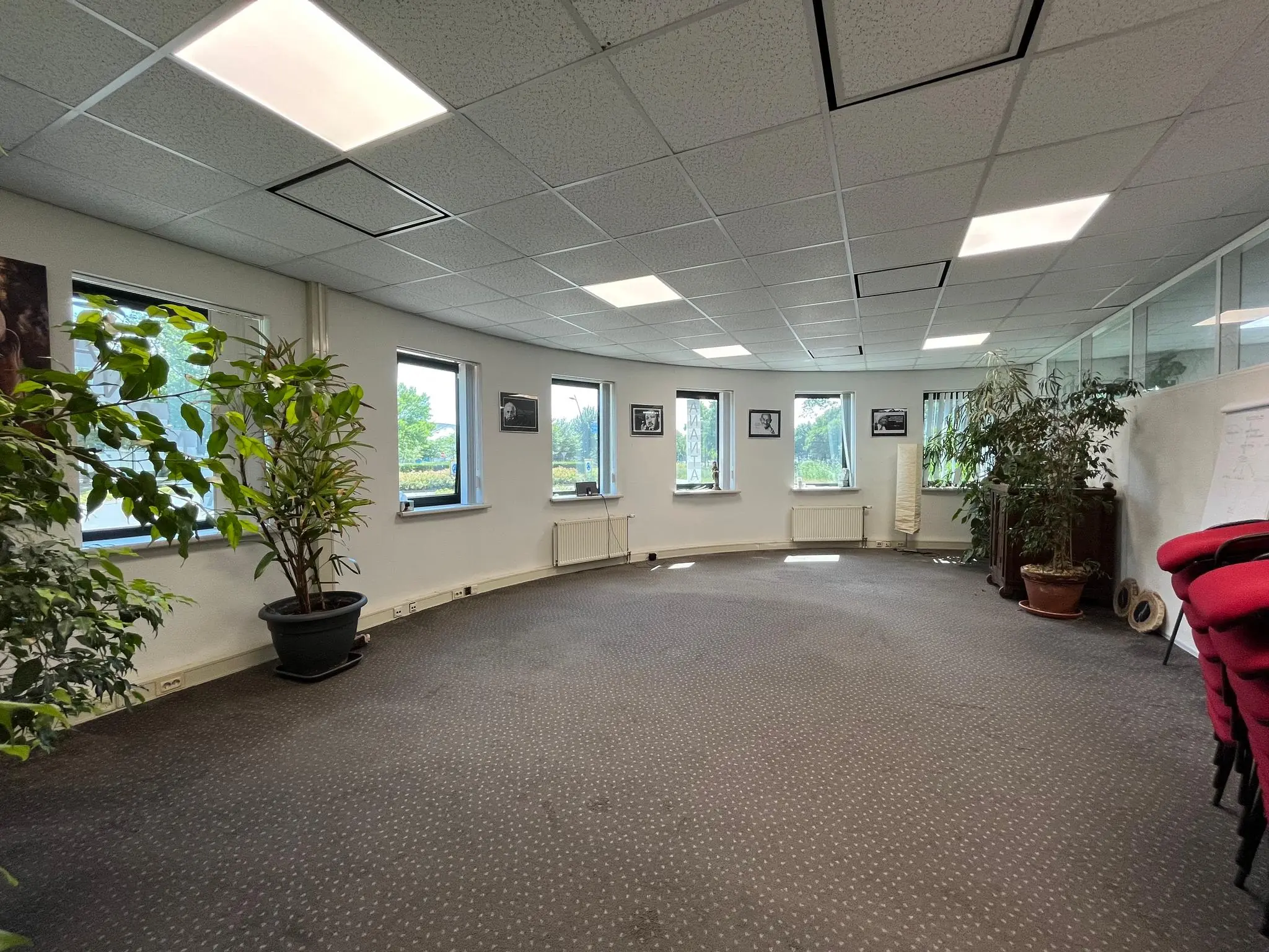 Ruime, ronde vergaderruimte met meerdere ramen, planten en rode stoelen, gelegen aan de Koningsweg.