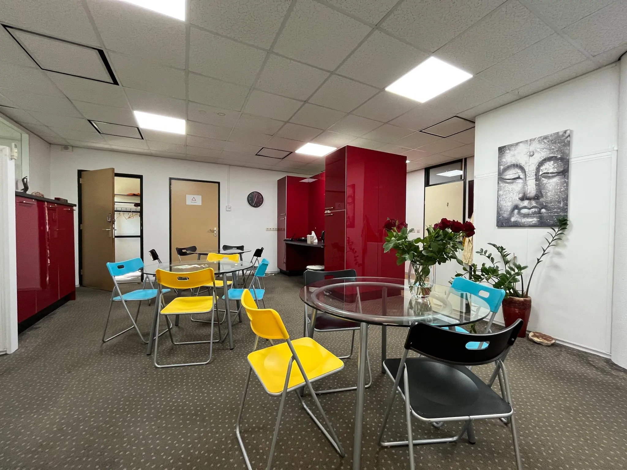 Kantoor kantineruimte aan de Koningsweg met kleurrijke stoelen, rode kasten en een Boeddha-schilderij aan de muur.