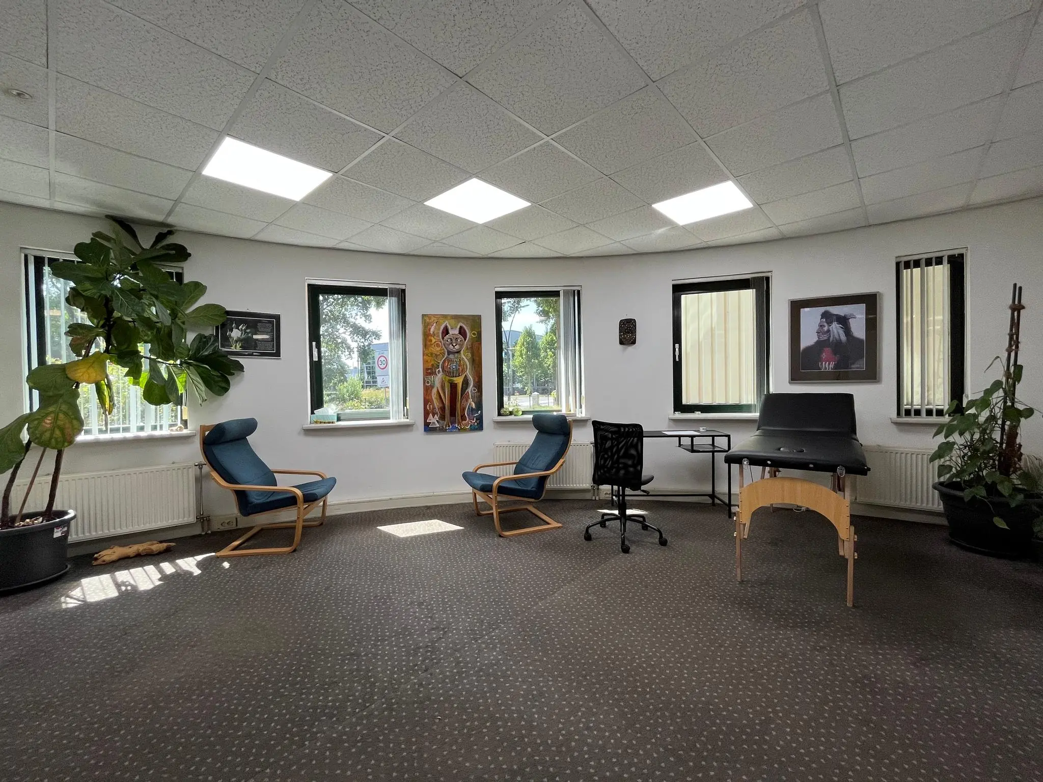 Moderne praktijkruimte aan de Koningsweg met zithoek, behandelbank en grote kamerplanten.