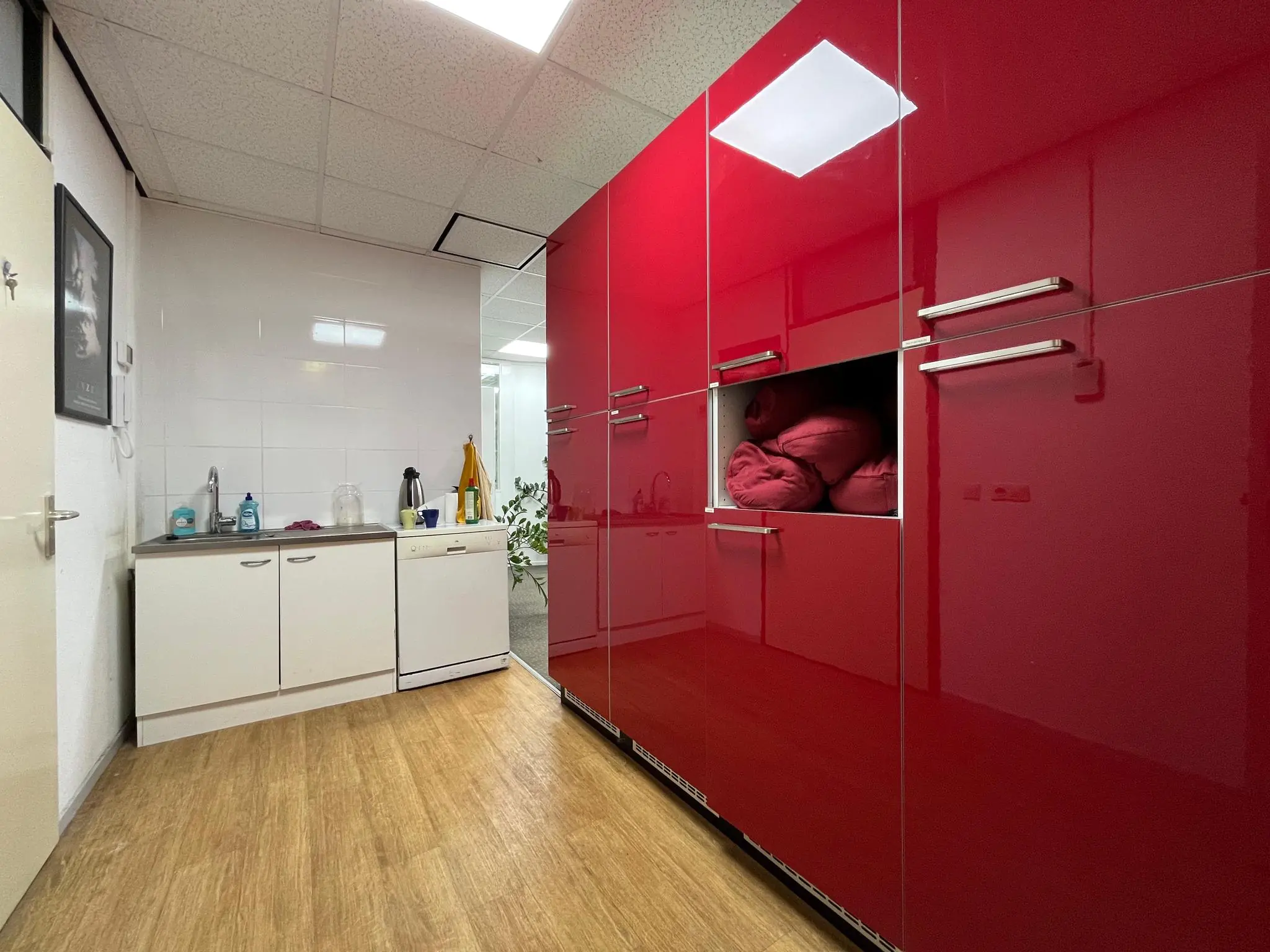 Kleine pantry met witte kasten en een groot rood wandmeubel met opbergvakken in een ruimte aan de Koningsweg.