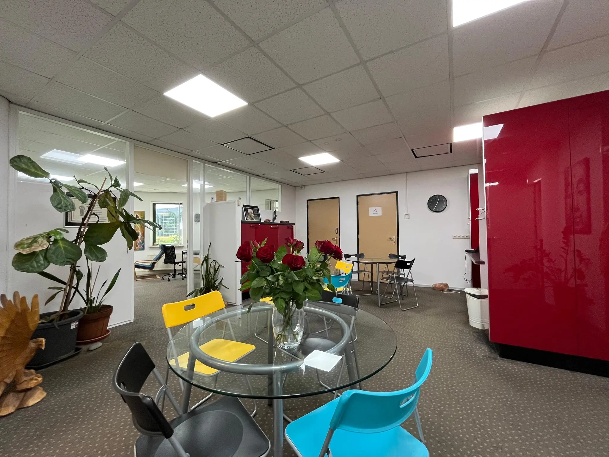 Kantoorruimte aan de Koningsweg met glazen wanden, kleurrijke stoelen en een ronde tafel met een vaas rode rozen.
