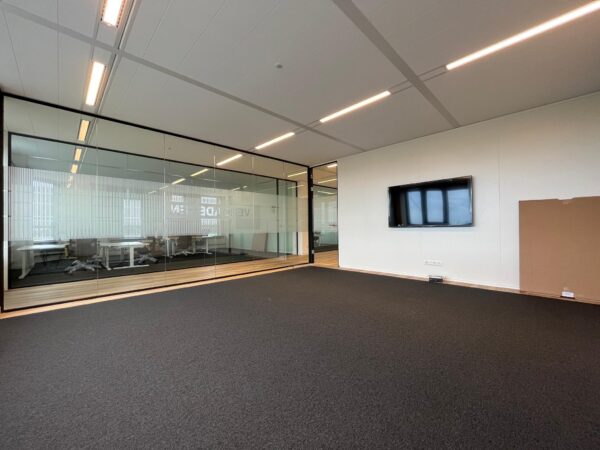 Moderne lege kantoorruimte met glazen vergaderruimte, wandmonitor en donker tapijt.