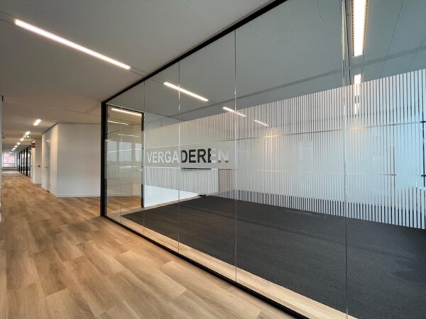 Glazen vergaderruimte met het woord "VERGADEREN" op de wand in een modern kantoorpand aan het Kosterijland.