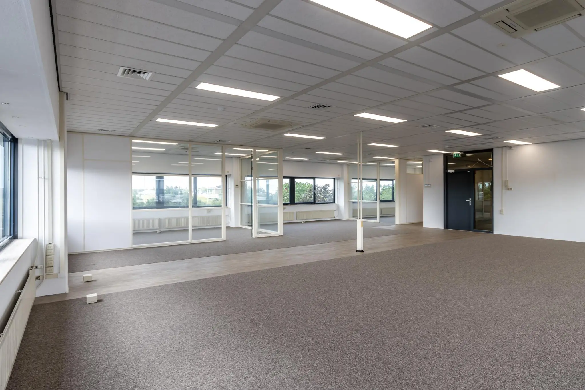 Lichte, lege kantoorruimte aan de Zonnebaan met glazen wanden en tapijtvloer.