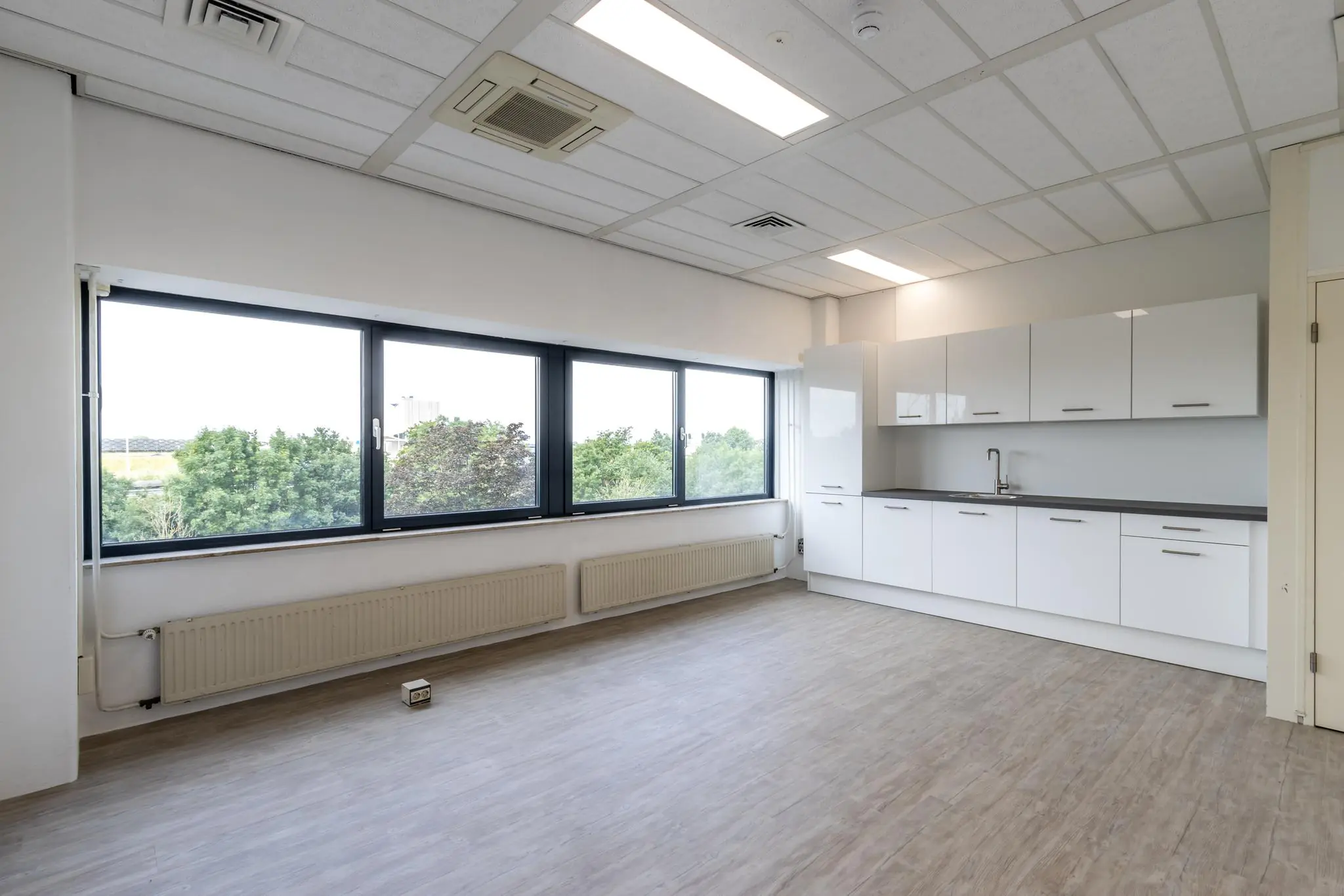 Lichte kantoorruimte aan de Zonnebaan met moderne pantry en grote ramen met uitzicht op groen.