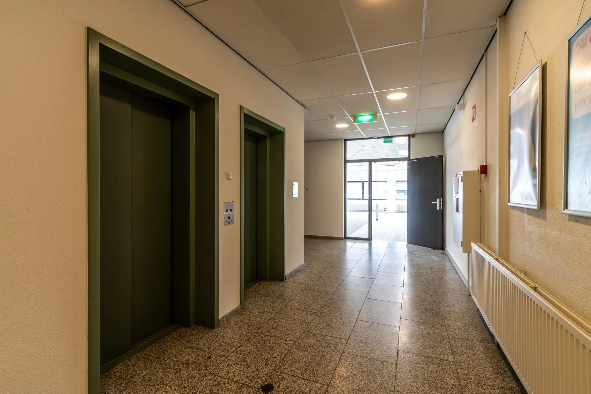 Hal met twee gesloten liften in een kantoorgebouw aan de Zonnebaan, met open deur naar een lichtere ruimte.