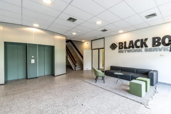 Moderne ontvangsthal van Black Box Network Services met zitgedeelte, liften en trap.