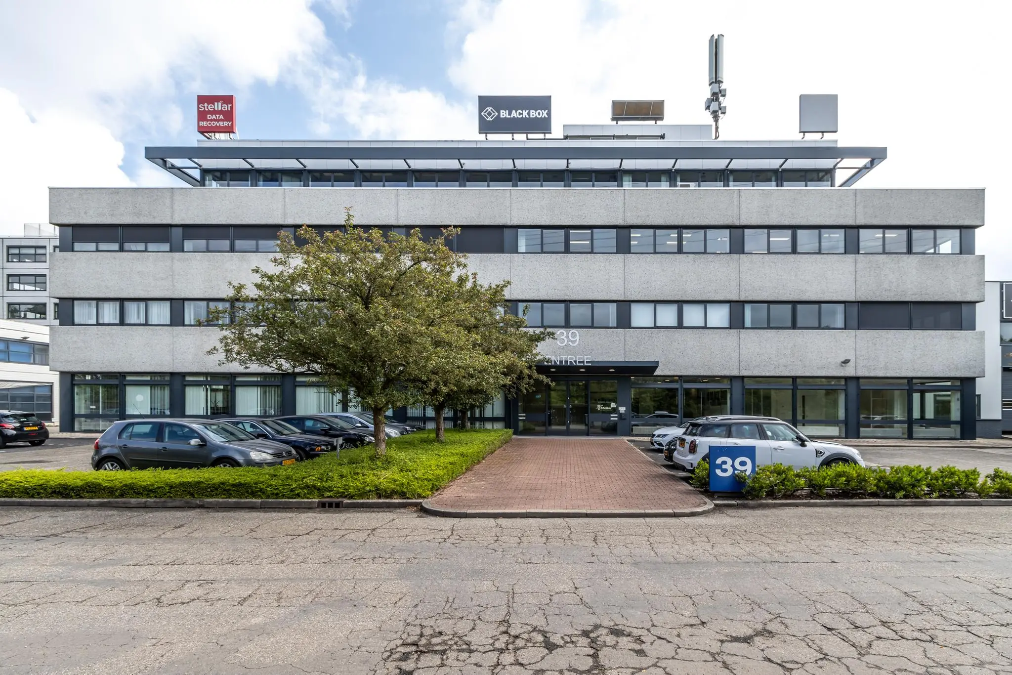 Vooraanzicht van een kantoorpand aan de Zonnebaan 39 met parkeergelegenheid en bomen voor de ingang.