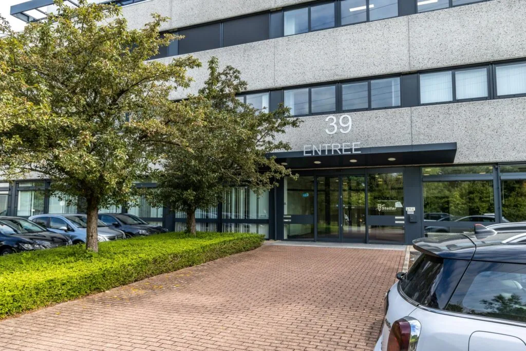 Ingang van kantoorpand aan de Zonnebaan 39 met parkeerplaatsen en bomen ervoor.