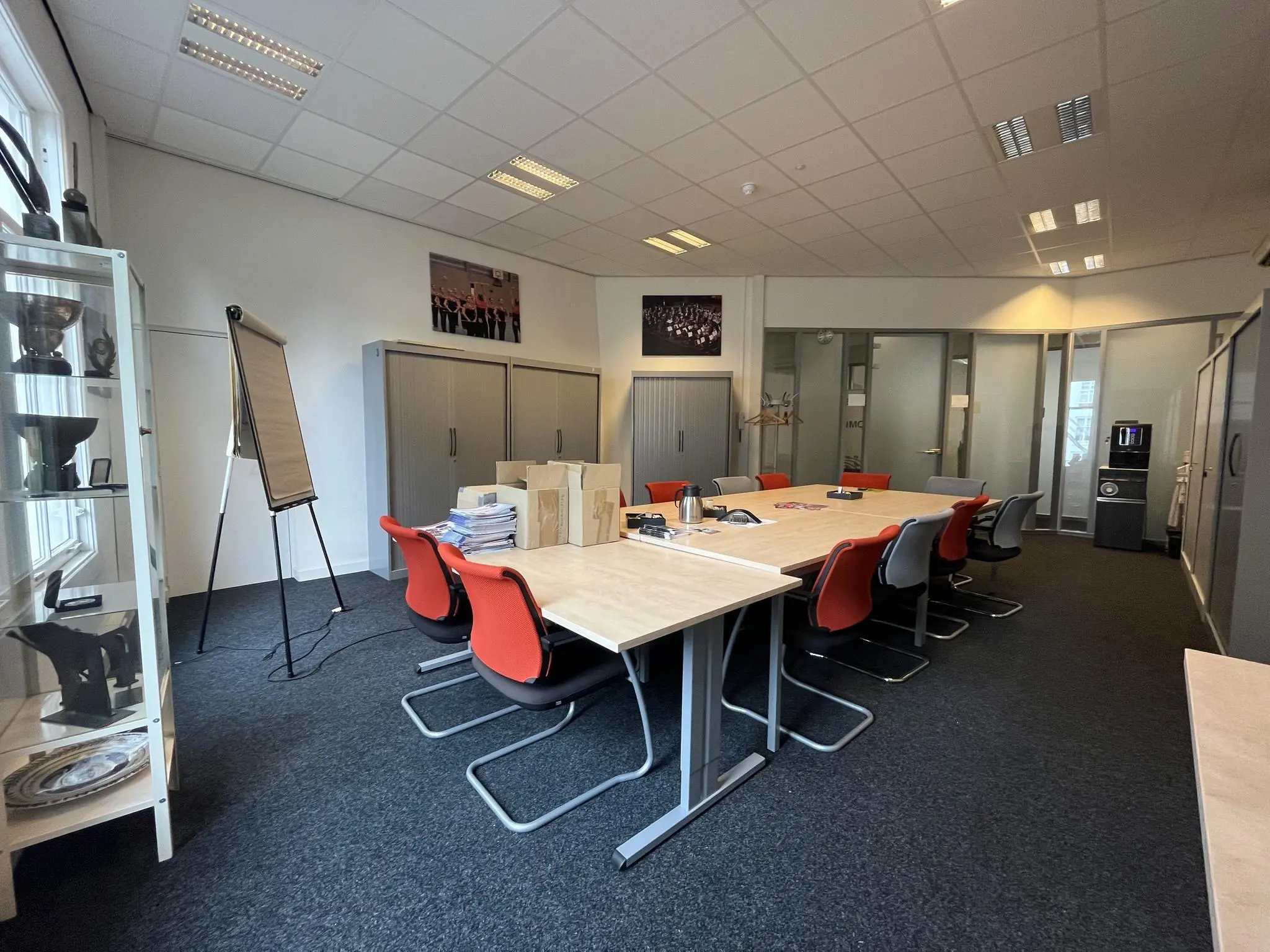 Vergaderruimte aan de Ganzenmarkt met lange tafel, rode en grijze stoelen, flip-over en een koffieautomaat.