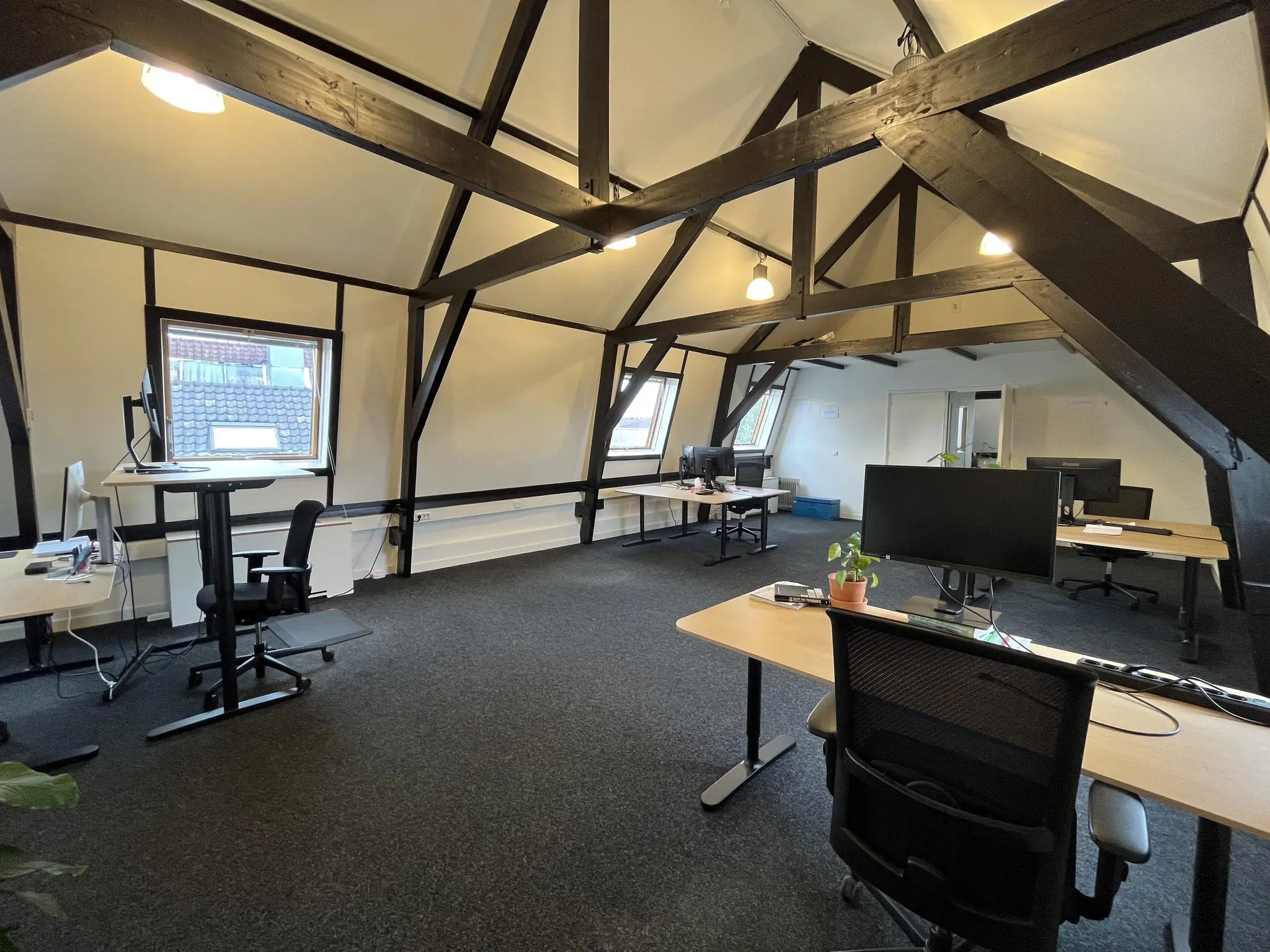 Modern kantoor met houten balken op een zolderverdieping aan de Ganzenmarkt, ingericht met bureaus en computerschermen.