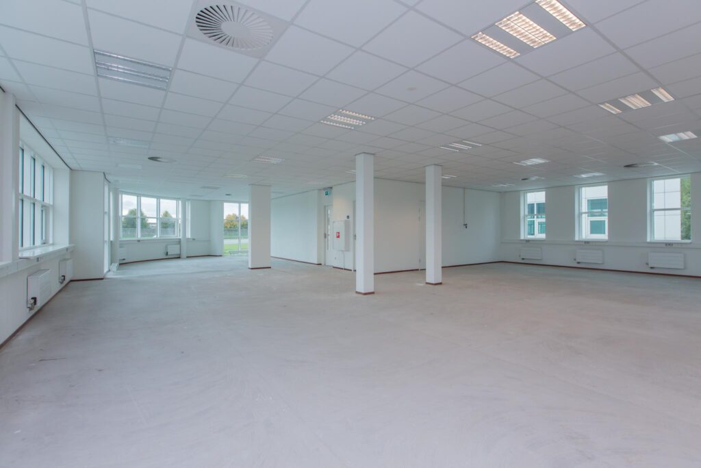 Lichte, lege kantoorruimte in het Rhijnspoor-gebouw met grote ramen en systeemplafond.