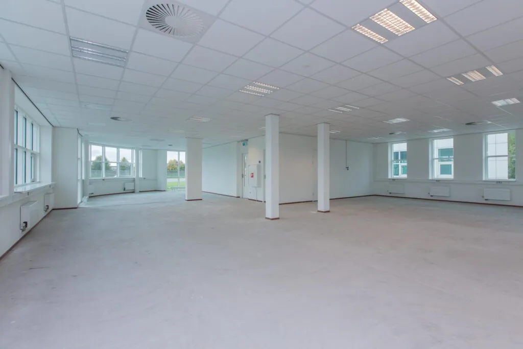 Lichte, lege kantoorruimte in het Rhijnspoor-gebouw met grote ramen en systeemplafond.