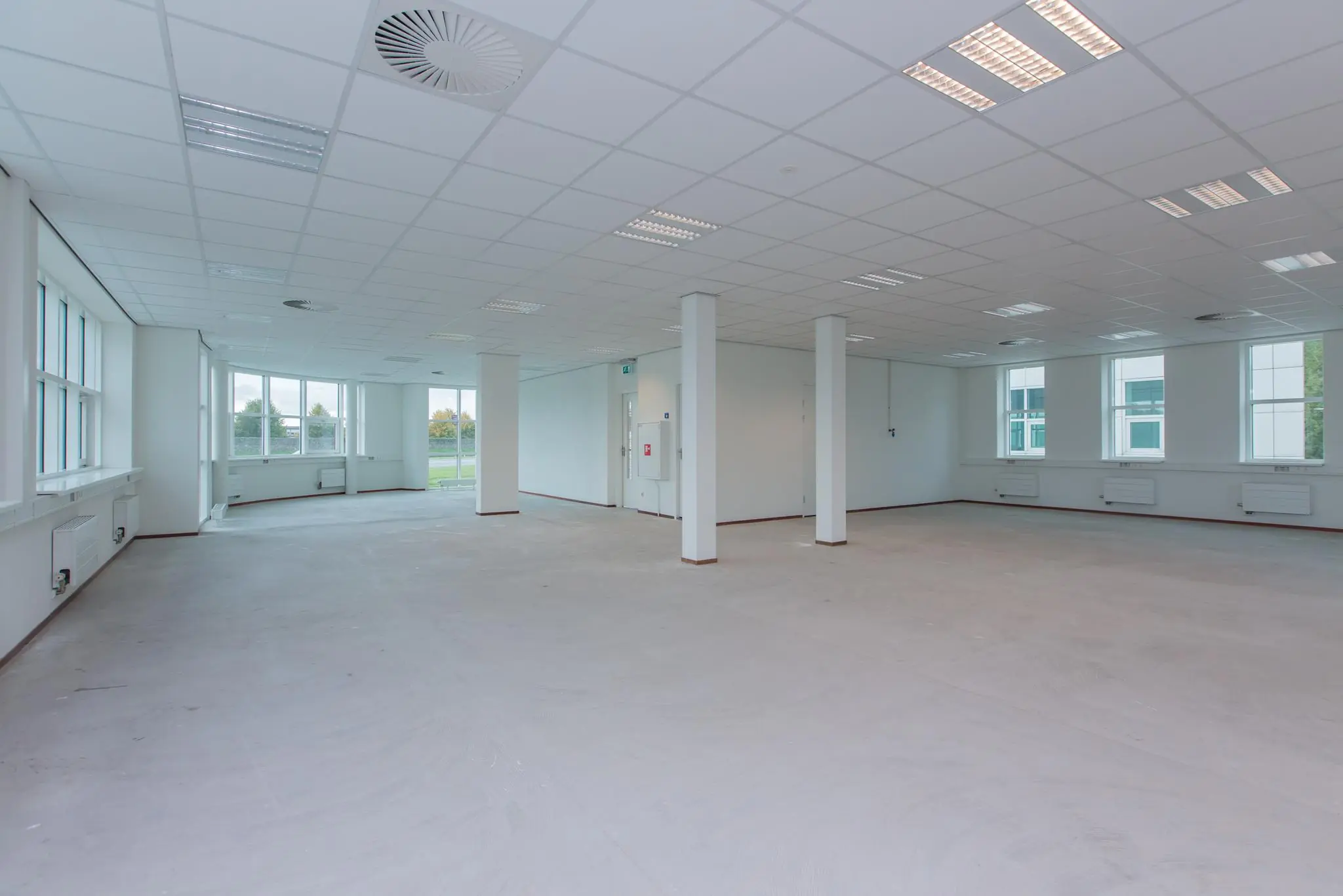 Lichte, lege kantoorruimte in het Rhijnspoor-gebouw met grote ramen en systeemplafond.