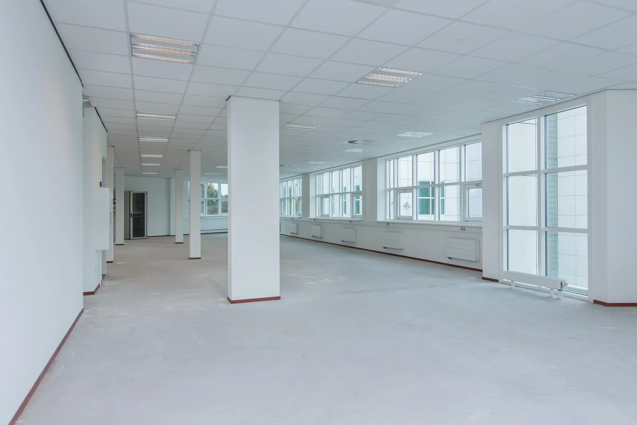 Leeg en licht kantoorpand aan het Rhijnspoor met wit afgewerkte muren en grote ramen.