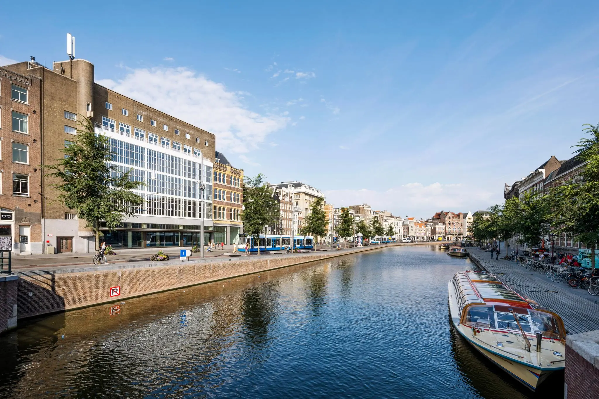 Zicht op het Rokin in Amsterdam met een rondvaartboot, een tram en historische gevels langs het water.