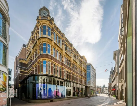 Historisch hoekpand aan het Rokin in Amsterdam met markante gevel en klok, gezien op een zonnige dag.