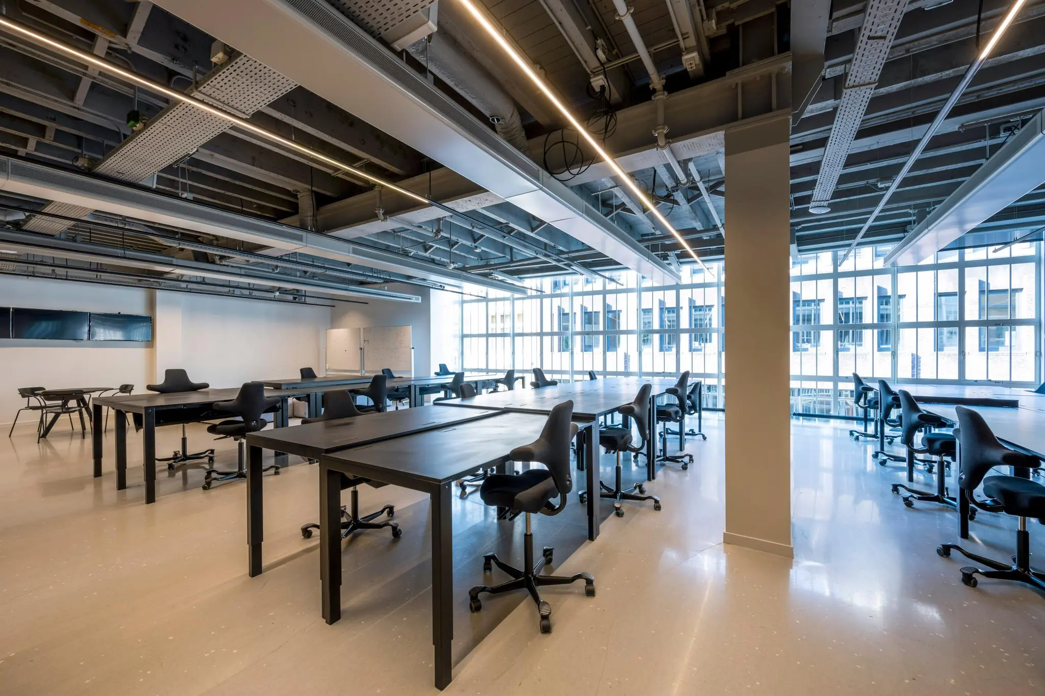 Ruime en moderne werkomgeving aan het Rokin met grote ramen, zwarte bureaus en verstelbare stoelen.