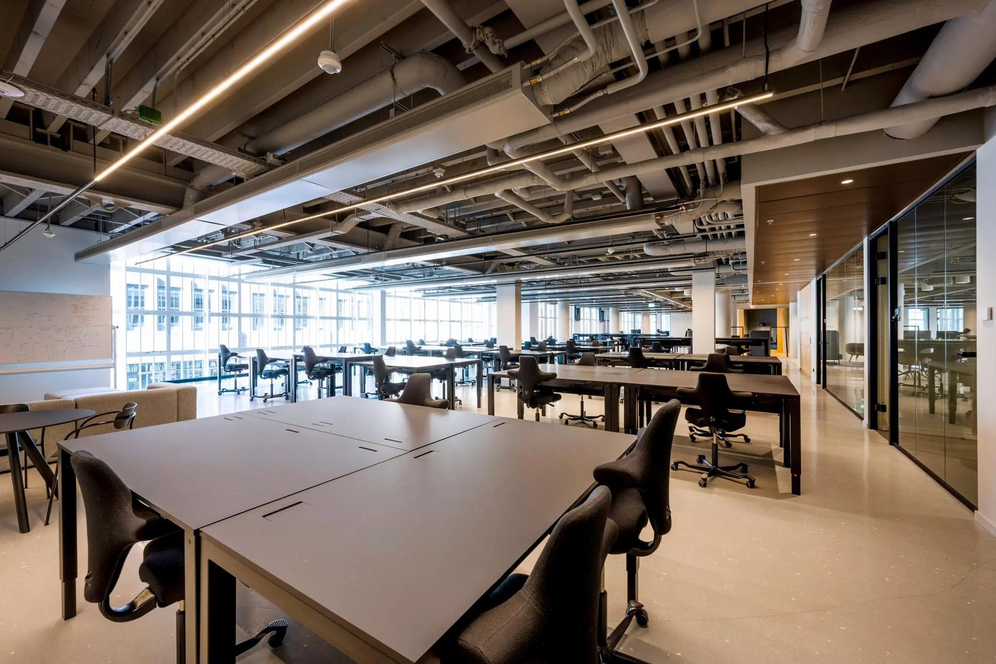 Moderne, open kantoorruimte aan het Rokin met lange bureaus, ergonomische stoelen en glazen vergaderruimtes.