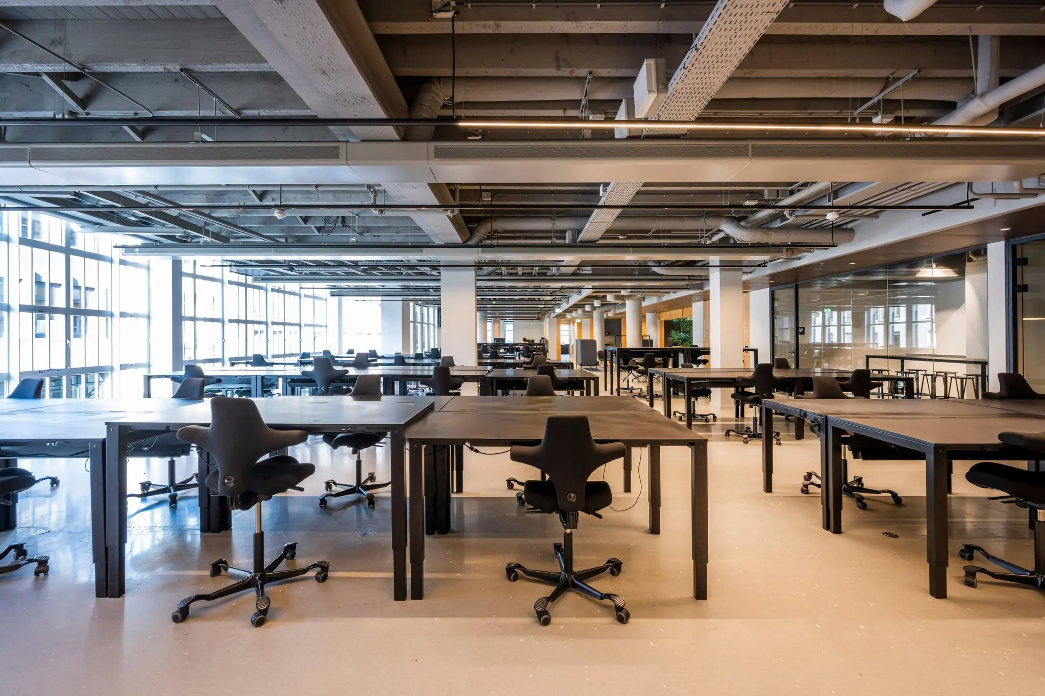 Moderne, open kantoorruimte aan het Rokin met lege zwarte bureaus en ergonomische bureaustoelen.
