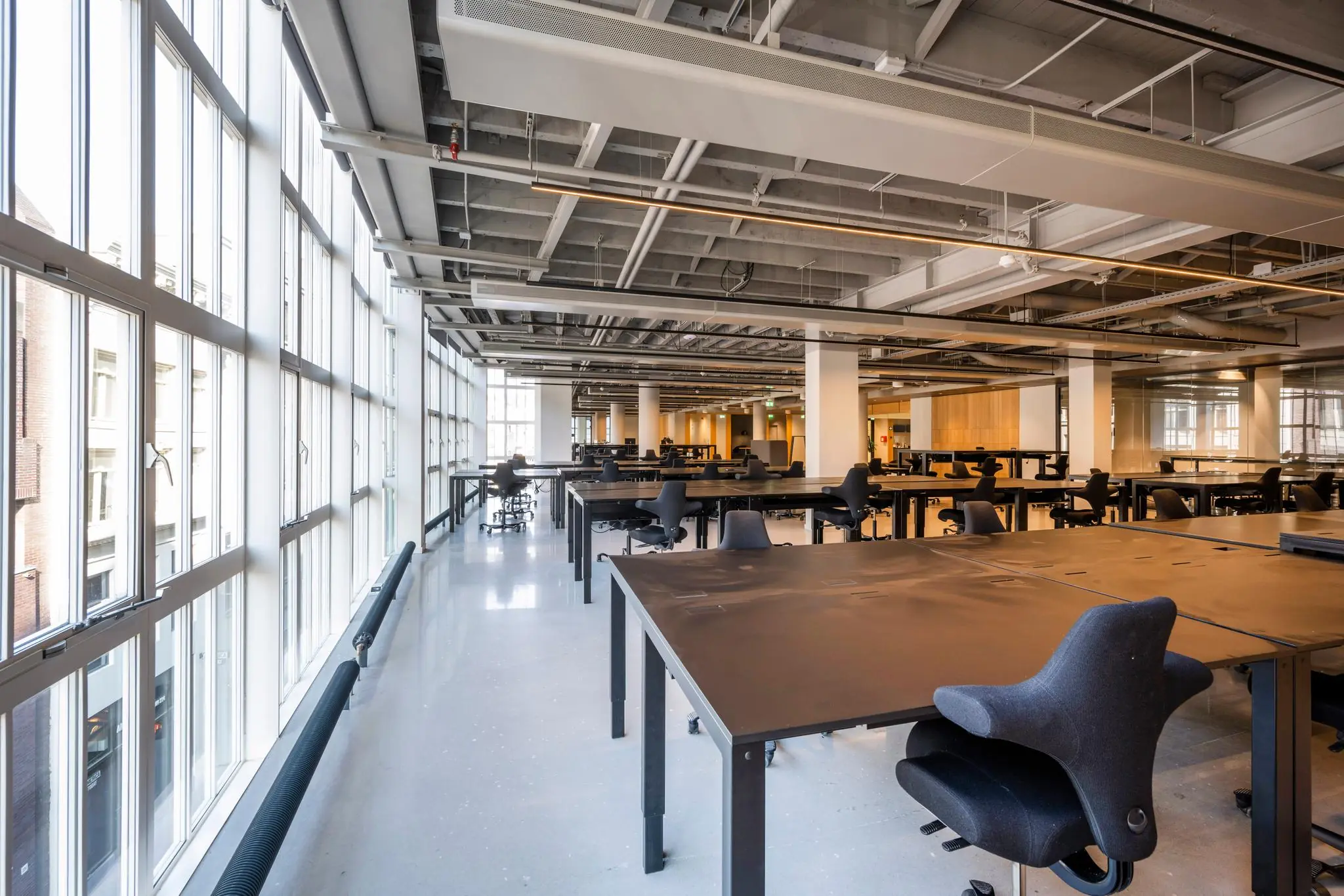 Ruim en modern kantoorinterieur aan het Rokin met grote ramen en lege werkplekken.