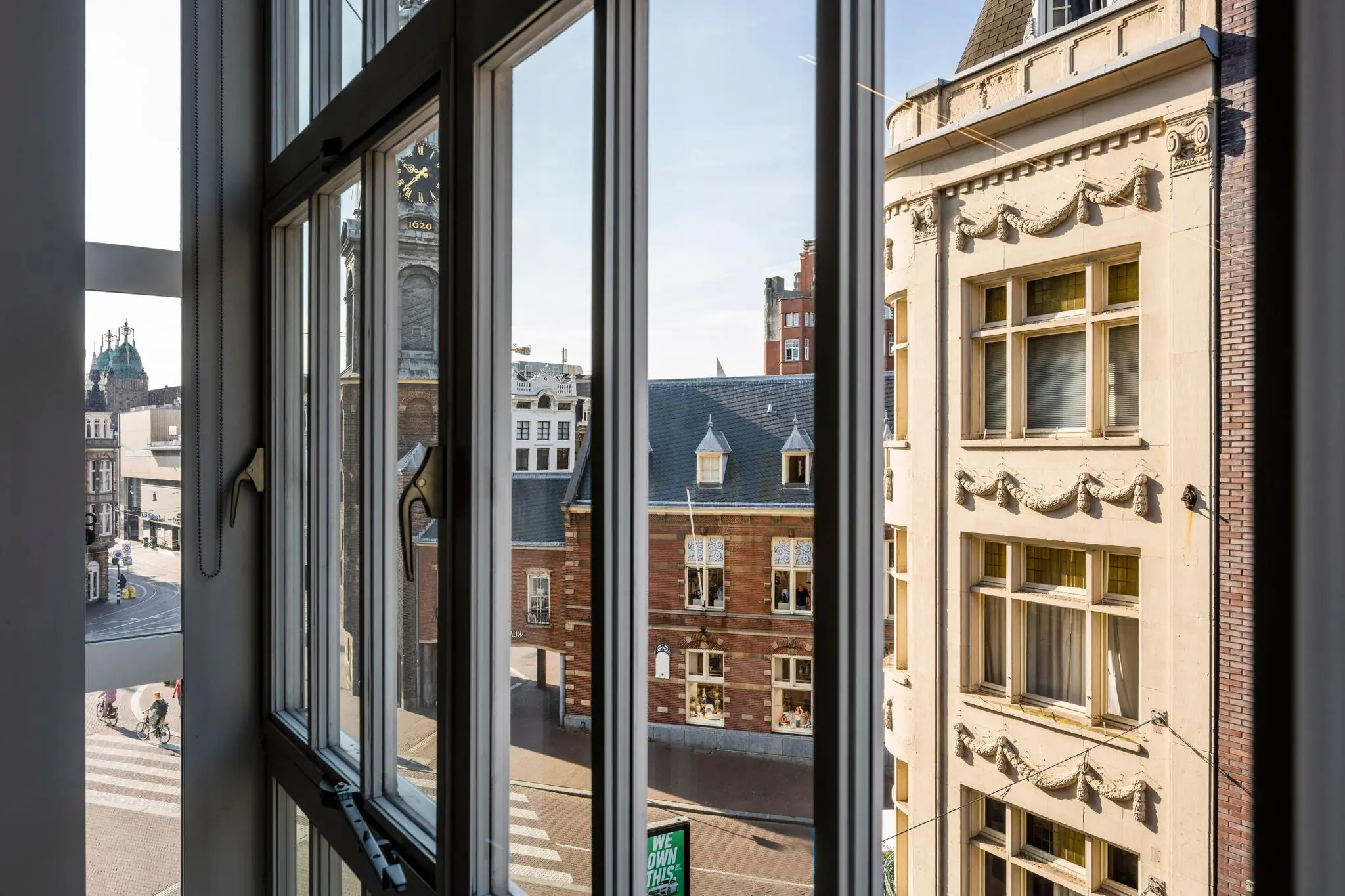 Uitzicht door een raam op het Rokin in Amsterdam met historische gevels en een klokkentoren.