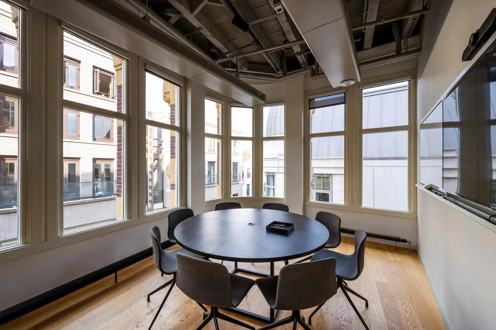Vergaderruimte met ronde tafel en acht stoelen in een modern kantoor aan het Rokin met uitzicht op omliggende gebouwen.