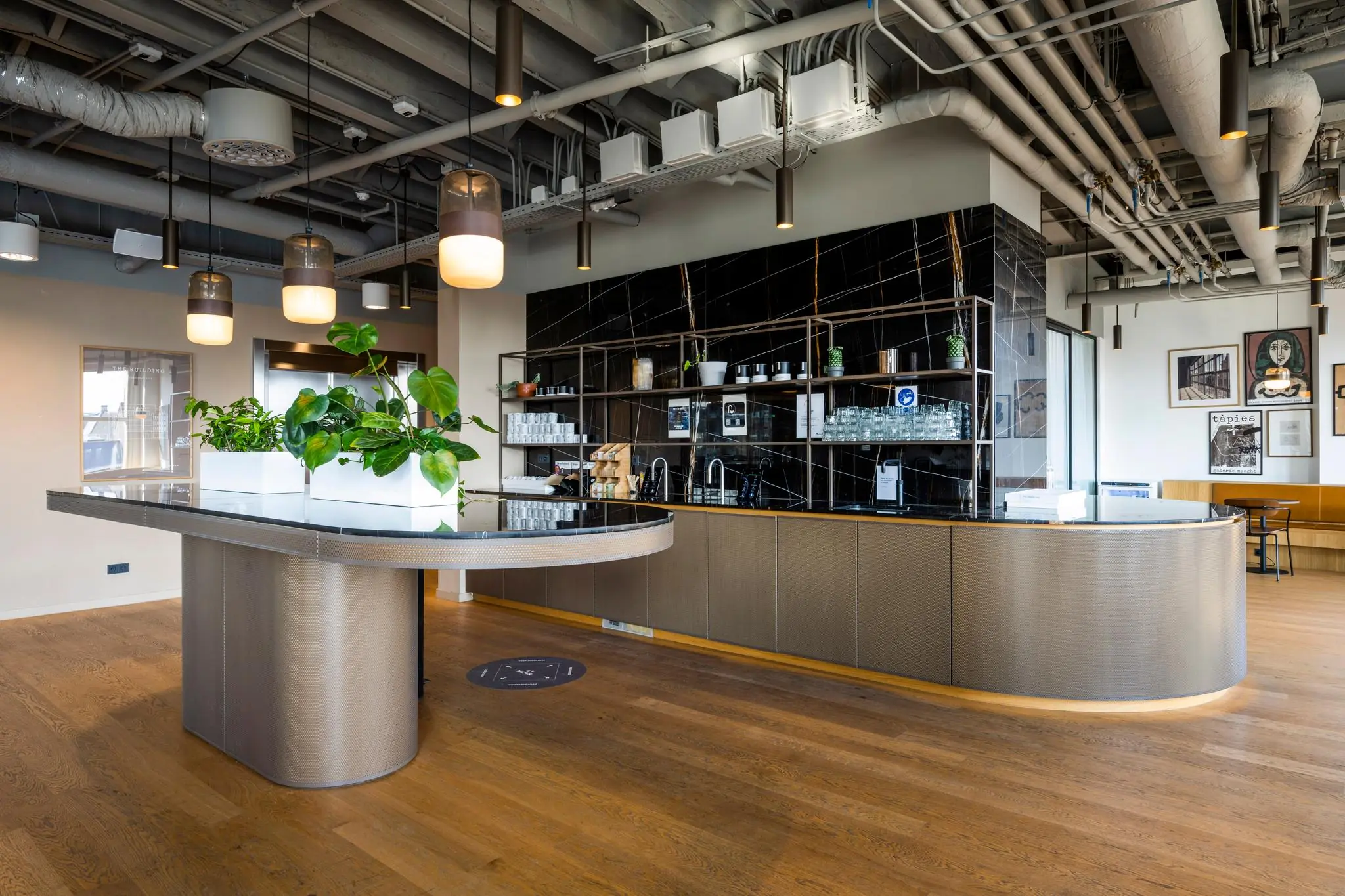 Moderne koffiekeuken met een zwart marmeren achterwand, hanglampen, planten en houten vloer in een kantoor aan het Rokin.