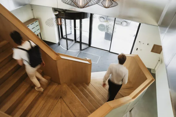 Twee mensen lopen op een houten trap in de entreehal van HNK Amsterdam Schinkel.