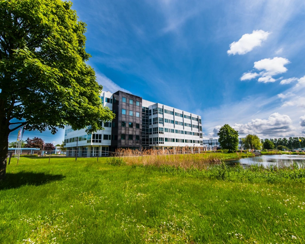 Modern kantoorgebouw aan de Bolderweg 2a in Almere, omgeven door groen en een vijver onder een blauwe lucht.