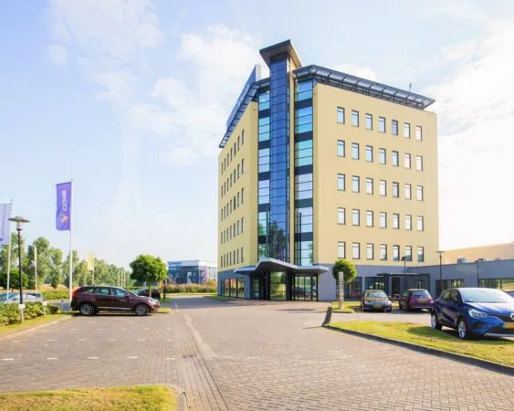 Modern kantoorgebouw aan de Pascallaan 60-78 in Lelystad met parkeerplaatsen en vlaggen op het terrein.