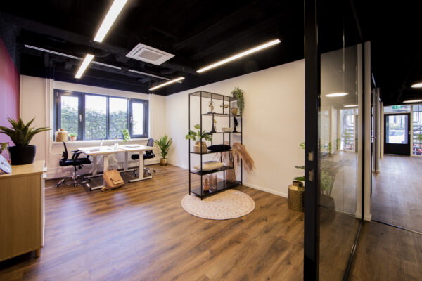 Modern kantoor met houten vloer, witte muren, een bureau bij het raam en een open rek met decoraties.