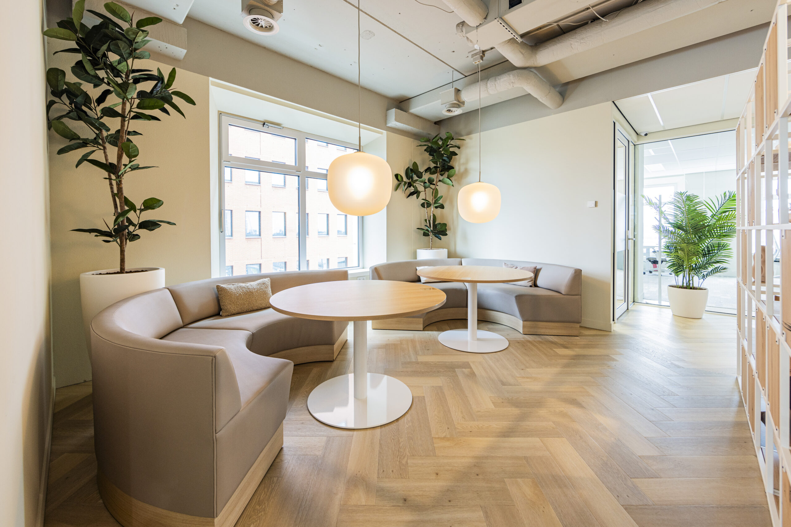 Een modern kantoor in Rotterdam met ronde banken, houten tafelbladen en grote kamerplanten.