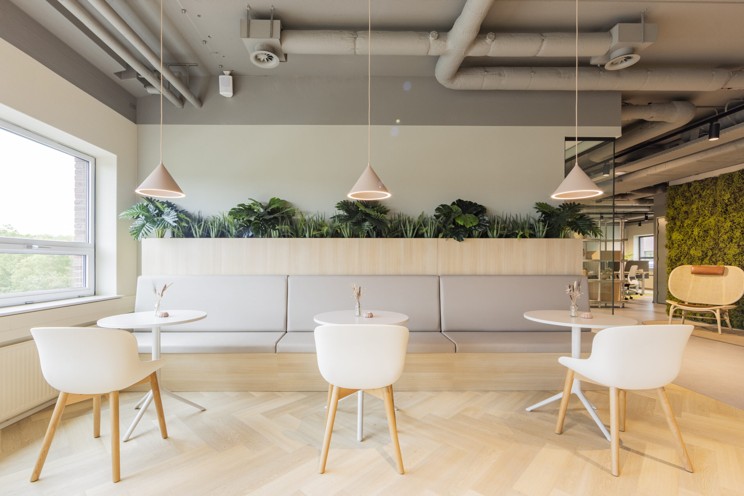 Een moderne, licht ingerichte lunchruimte met witte stoelen, ronde tafels en veel groen.