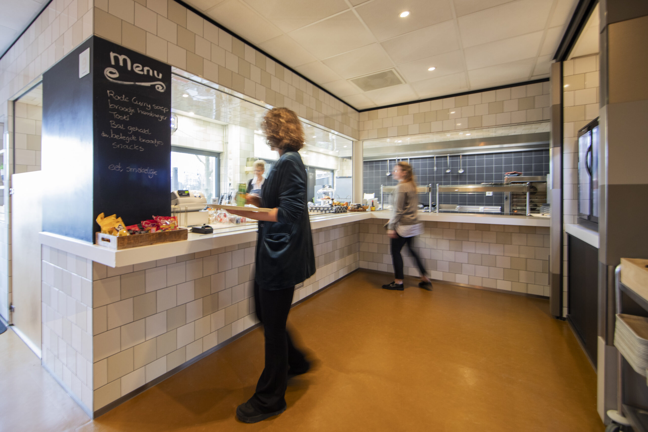 Een moderne restaurantruimte met een menu op een bord en mensen die eten bestellen en ophalen.