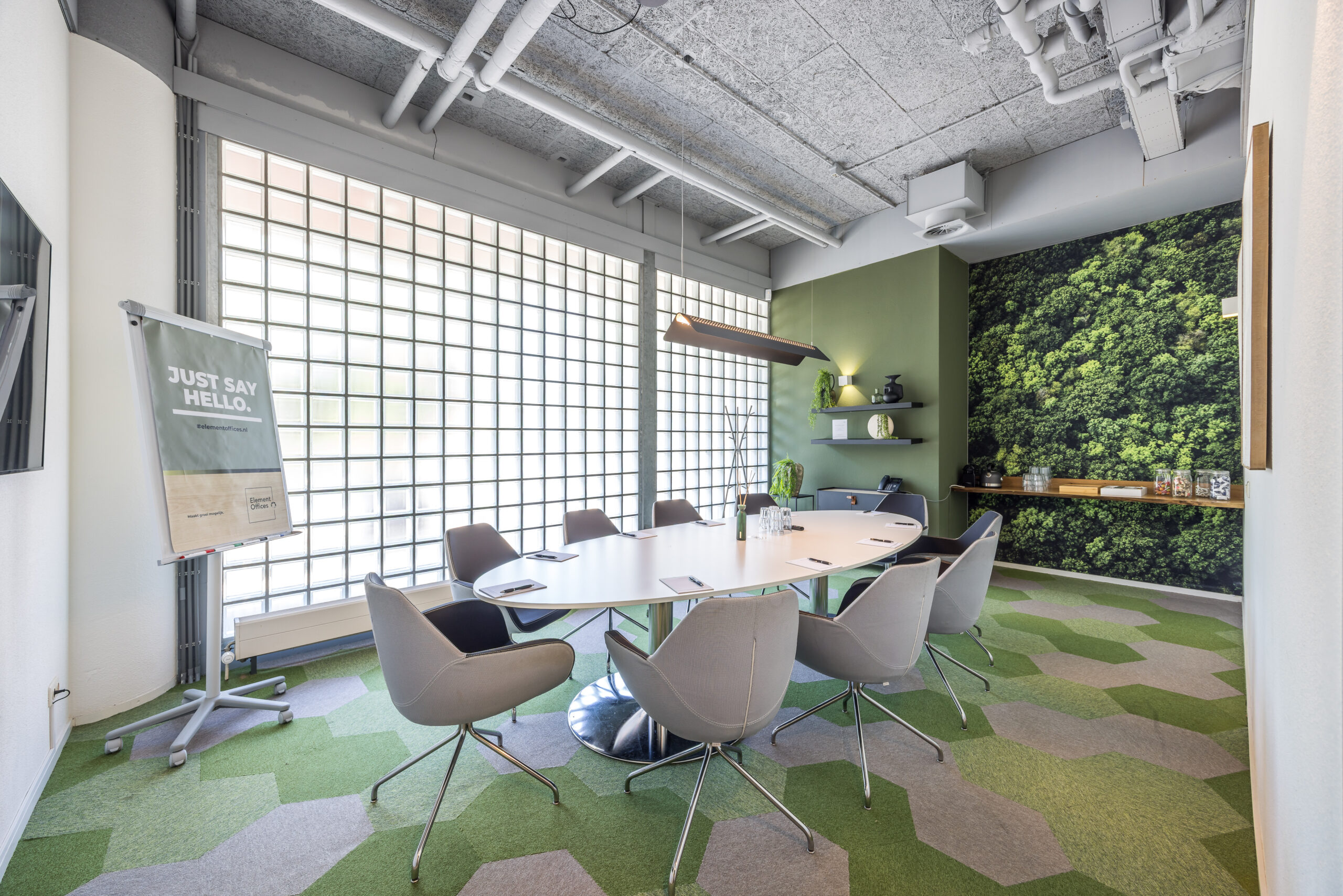 Een moderne vergaderruimte met een ovale tafel, comfortabele stoelen en een groene wanddecoratie.