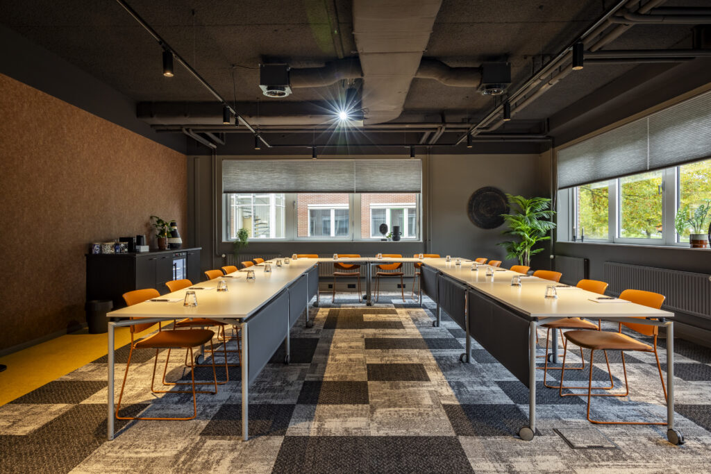 Een moderne vergaderzaal met tafels en oranje stoelen, ingericht voor een zakelijke bijeenkomst.