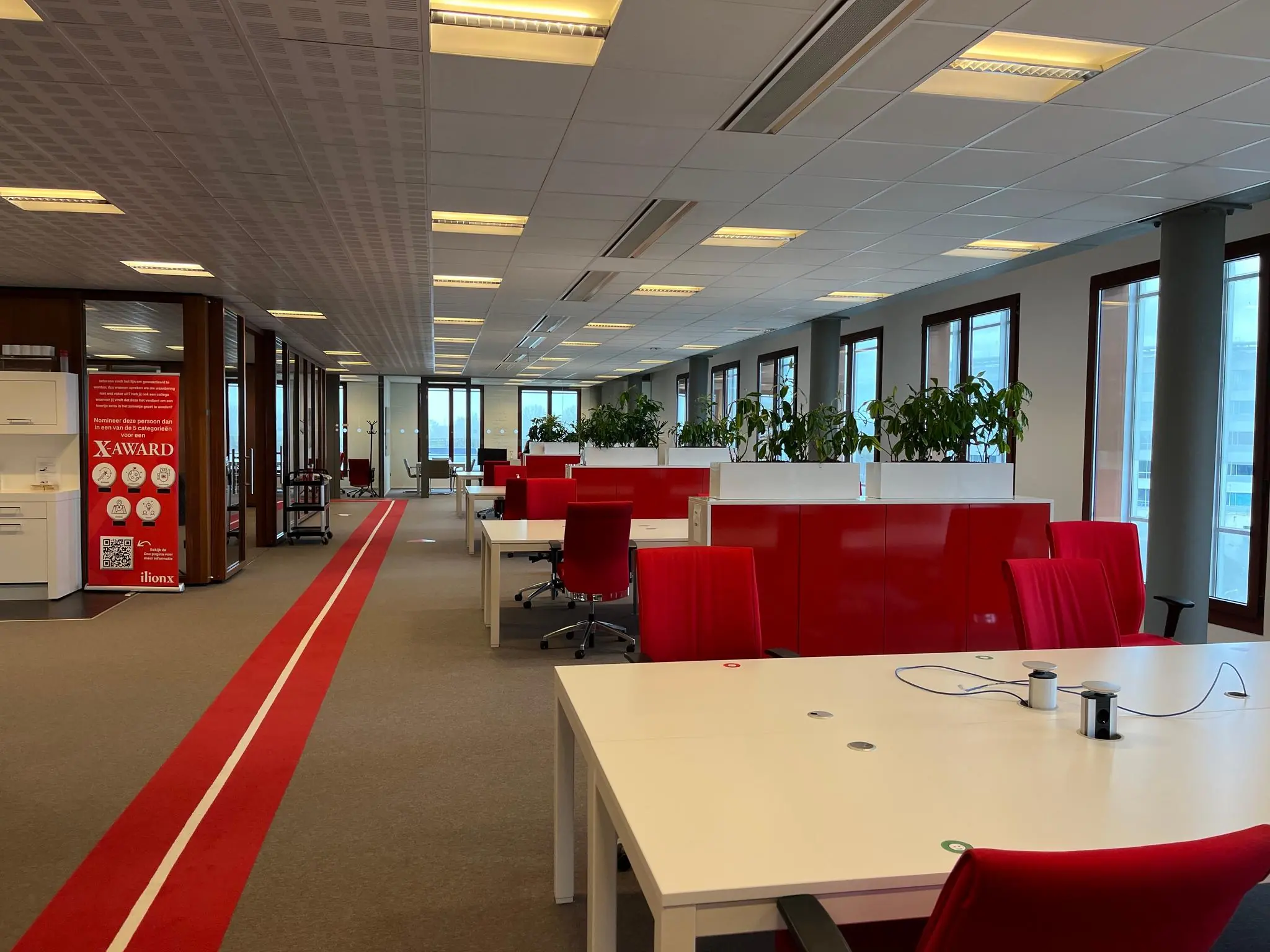 Moderne kantoorruimte aan de Hondiuslaan met rode accenten, flexwerkplekken en groene planten bij de ramen.