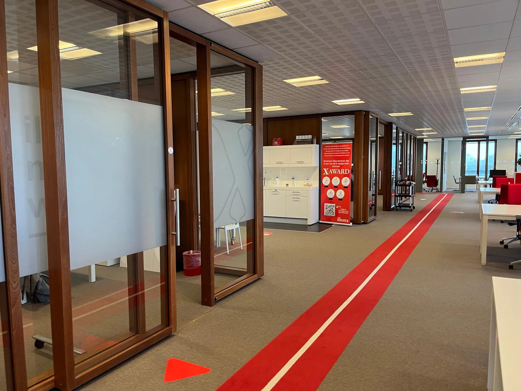 Modern kantoorinterieur aan de Hondiuslaan met glazen vergaderruimtes, rode looppaden en een XAWARD-poster.