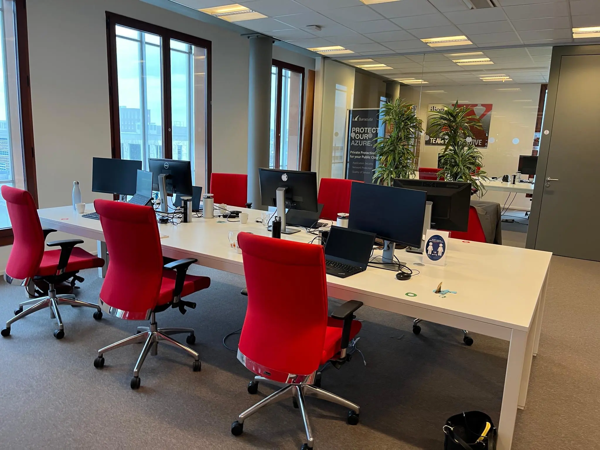 Modern kantoor op de Hondiuslaan met rode bureaustoelen, werkplekken met computerschermen en een glazen vergaderruimte op de achtergrond.