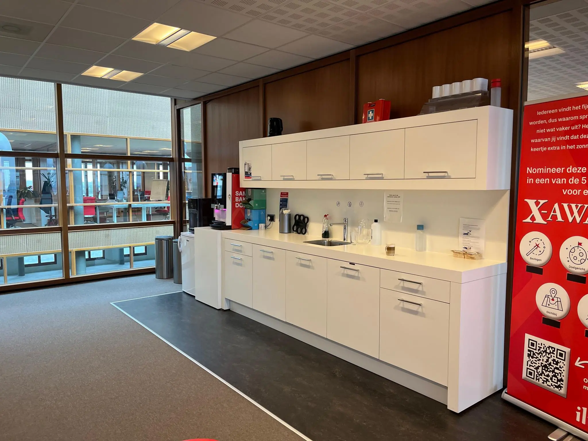 Bedrijfskantine met witte keuken, koffieautomaat en een rode X-Awards promotiebanner aan de Hondiuslaan.