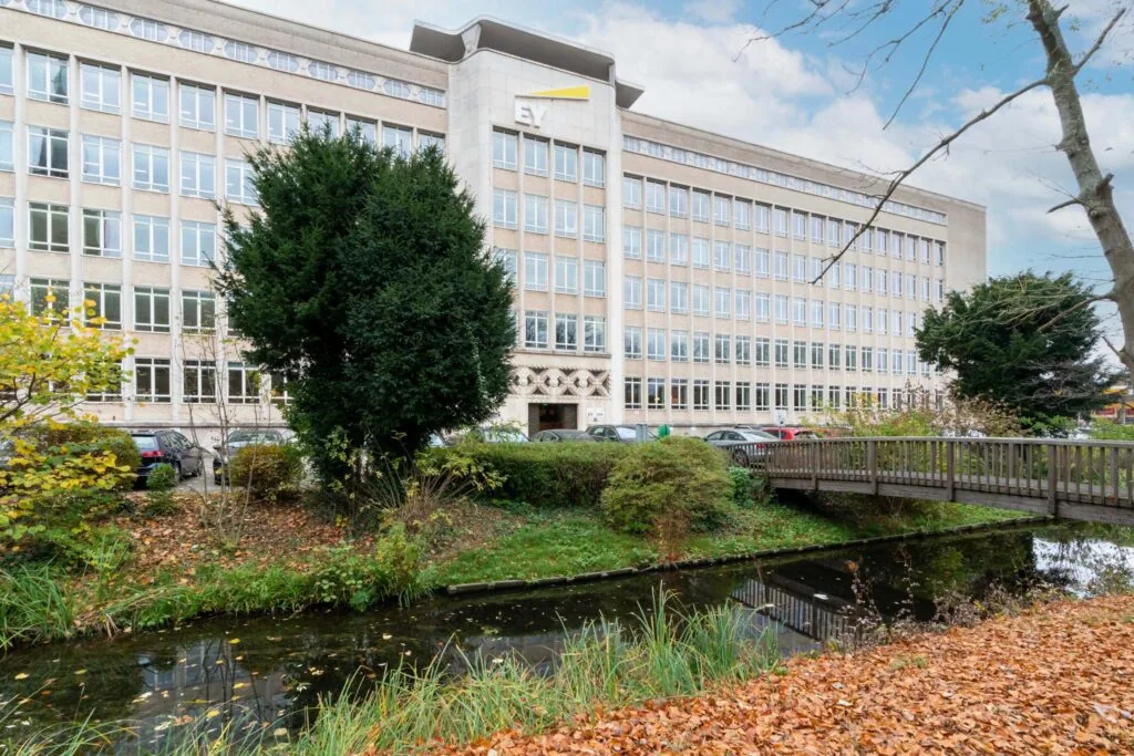 Kantoorgebouw van EY aan de Wassenaarseweg, gezien vanaf een brug over een vijver met herfstbladeren.