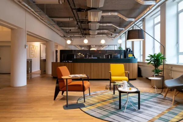 Moderne wachtruimte in het EY-kantoor aan de Wassenaarseweg met kleurrijke stoelen, een ronde vloerkleed en een houten receptiebalie.