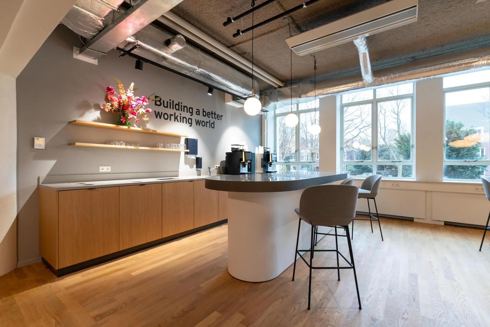 Moderne kantoor pantry aan de Wassenaarseweg met koffiehoek, hoge stoelen en slogan aan de muur.